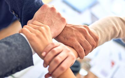 Four diverse hands joined together in a display of teamwork, symbolizing leadership and workplace culture change.