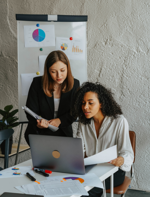 Two professionals collaborating in an office setting next to a presentation board displaying charts and graphs, focusing on leadership and management skill development using DiSC methodology.